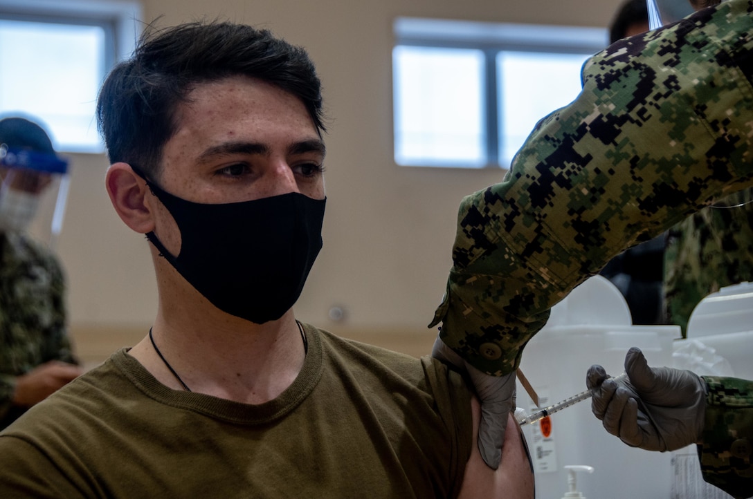 A sailor wearing a protective face mask receives a vaccine shot.