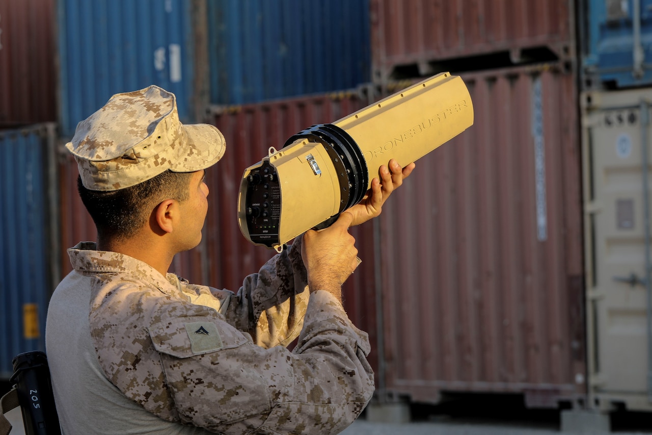 A service member points a large gun-like device into the air.