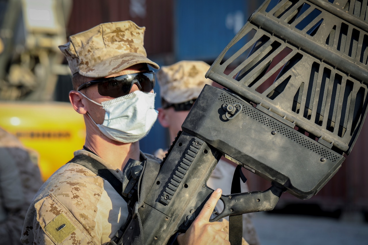 A service member holds a large gun-like device.
