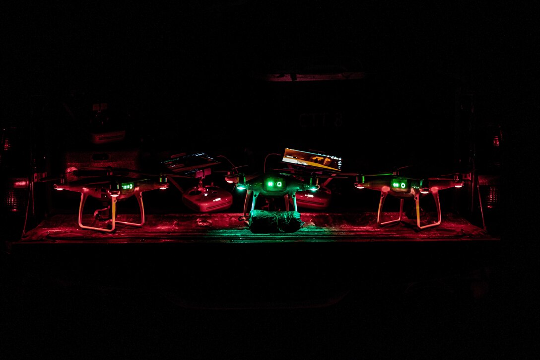 Several drones sitting on the ground light up at night.