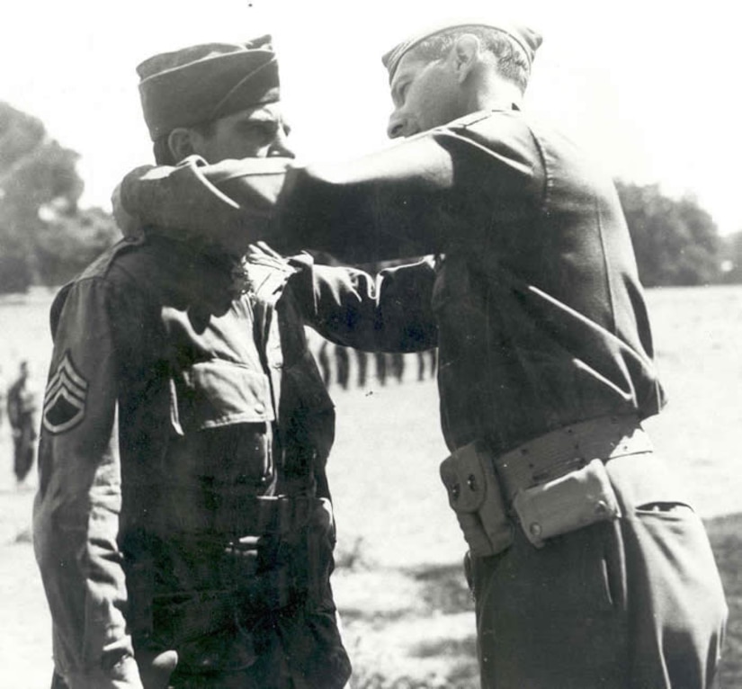 A uniformed man places a medal on a ribbon around the neck of another uniformed man.