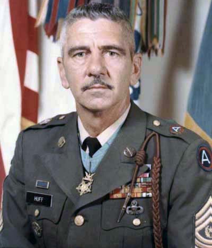 A man in service dress uniform wearing a medal around his neck looks at the camera.