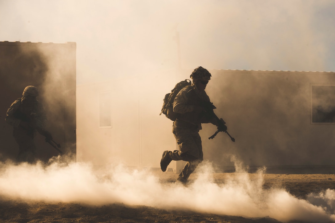 Marines move through dust holding weapons.
