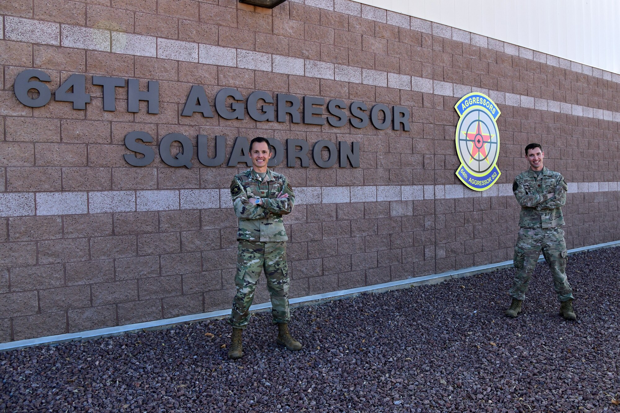 Maj. Scott Hollister and Maj. Jason Brosseau, 26th Space Aggressor Squadron, VADER-1, stand in front of the 64th Space Aggressor Squadron building Feb. 2, at Nellis Air Force Base, Nevada. Reservists, Hollister and Brosseau, deliver expertise in satellite communication and GPS electronic attack, and how those effects are integrated with air, air defense, and cyber to help create realistic enemy threats and tactics for those participating in Red Flag 21-1.