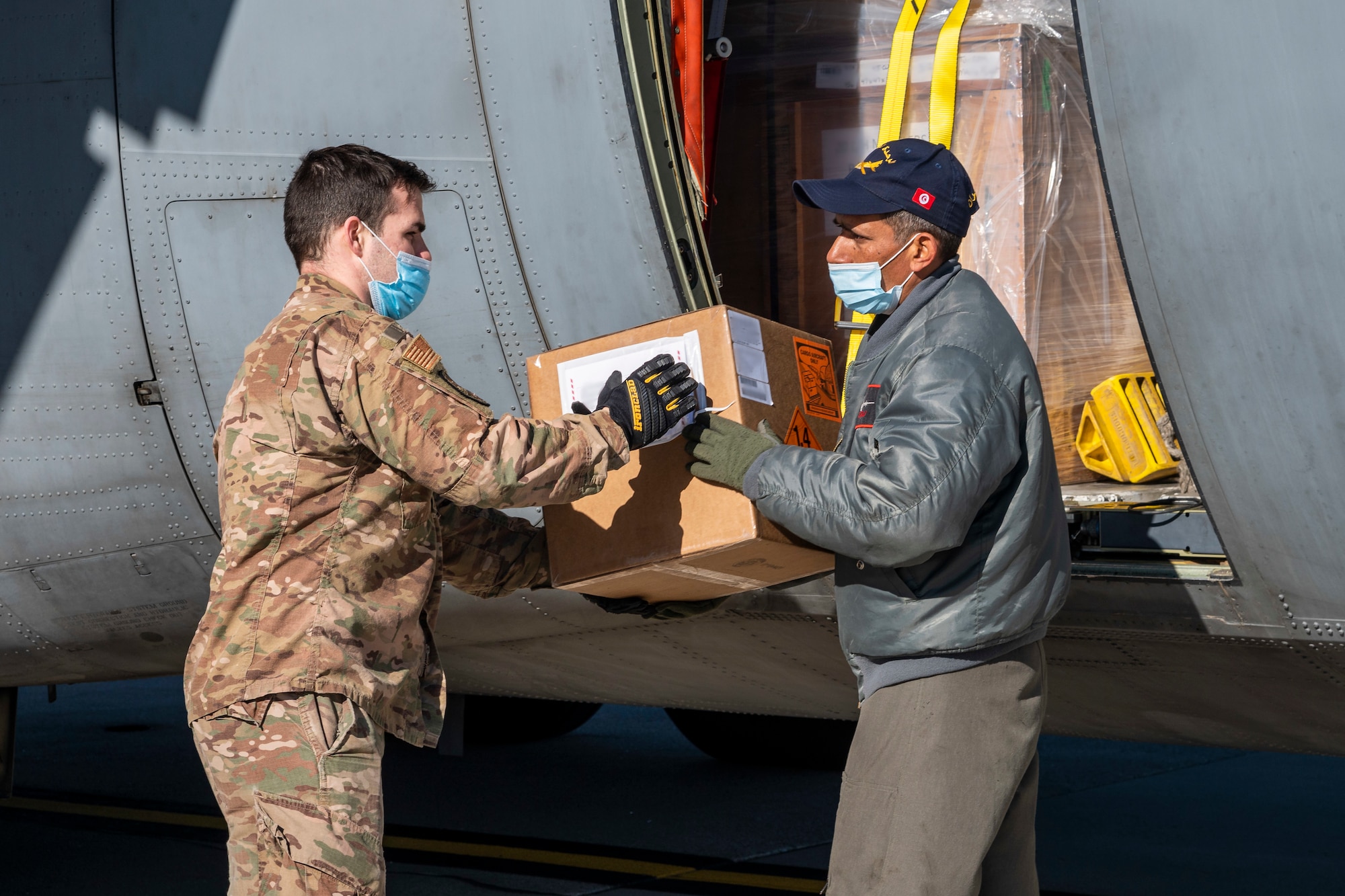 Staff Sgt. Deric Sexton, 436th Aerial Port Squadron load planner, delivers foreign military sales cargo to a Tunisian air force airman at Dover Air Force Base, Delaware, Jan. 28, 2021. The U.S. and Tunisia have enjoyed strong diplomatic relations for over 200 years, a special bond first enshrined when the two countries signed the Treaty of Peace and Friendship in 1797. Tunisia was among the first to recognize the newly independent U.S. during that time. Due to its strategic geographic location, Dover AFB supports approximately $3.5 billion worth of FMS operations annually. (U.S. Air Force photo by Senior Airman Christopher Quail) (This image was altered for security purposes by blurring identification on cargo)