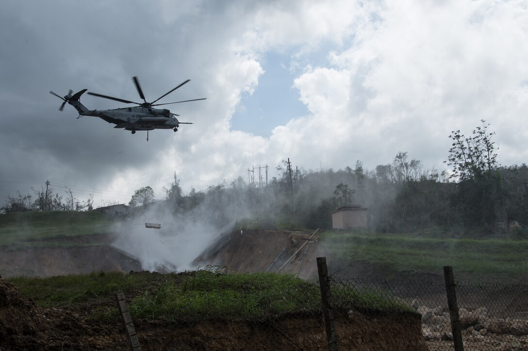 A U.S. Marine Corps CH53, Sikorsky Sea Stallion heavy-lift transport helicopter, lifts five-ton Jersey barriers into the Guajataca Dam, in Guajataca, PuertoRico, Monday. USACE is assisting the Puerto Rico Electric Power Authority in efforts to reduce the risk from Guajataca Dam to downstream communities by performing structural assessments, and planning and coordinating aircraft, equipment and materials to temporarily shore up the damaged spillway.
The emergency repairs to the dam is an interagency effort to mitigate damages caused by the heavy rains and inflows from HurricaneMaria. This emergency effort will be followed by a temporary and finally permanent fix in the future.