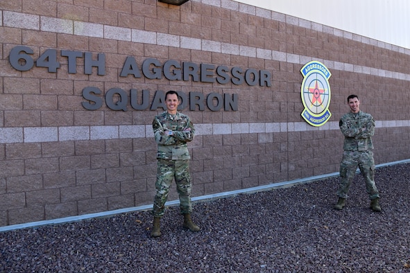 Maj. Scott Hollister and Maj. Jason Brosseau, 26th Space Aggressor Squadron, VADER-1, stand in front of the 64th Aggressor Squadron building Feb. 2, at Nellis Air Force Base, Nevada. Reservists, Hollister and Brosseau, deliver expertise in satellite communication and GPS electronic attack, and how those effects are integrated with air, air defense, and cyber to help create realistic enemy threats and tactics for those participating in Red Flag 21-1.
