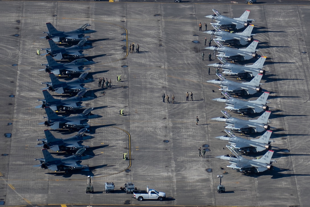 Two rows of F-16 aircraft are parked on a ramp.