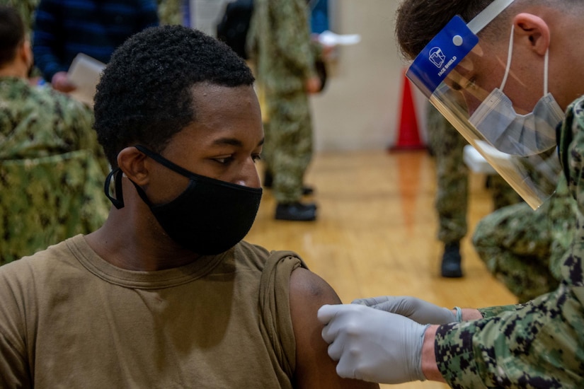 A sailor wearing a protective face mask receives a vaccine shot in the arm.