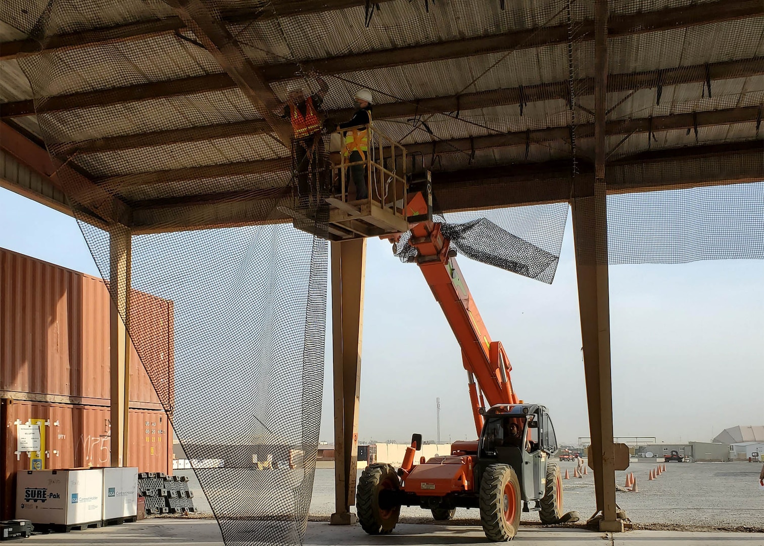 Ted Adams, left, works with Jhunar Medenilla in a lift basket used to help them hang netting to keep out birds that were fouling up a receiving area at DLA Disposition Services at Camp Arifjan.