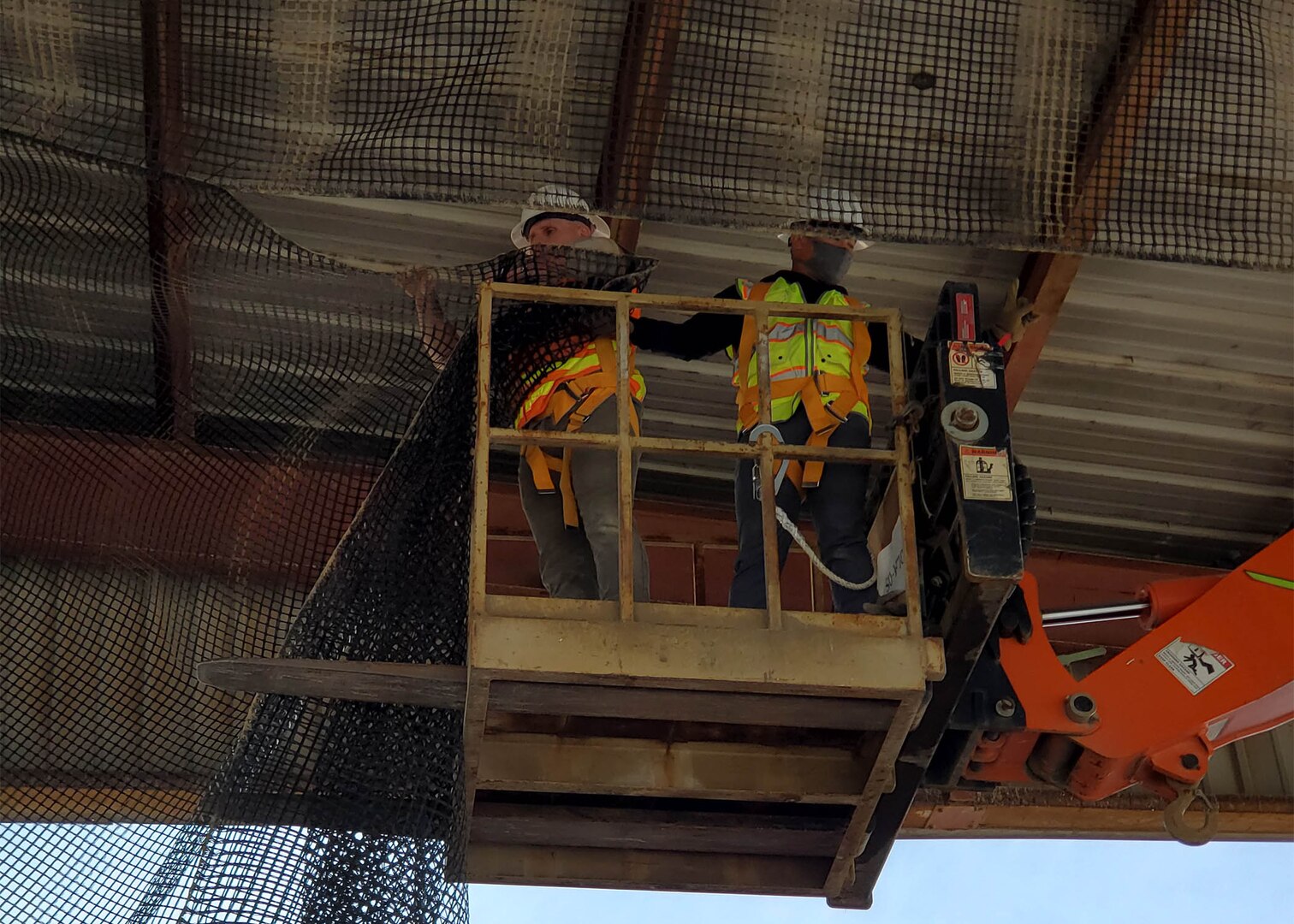 Jhunar Medenilla, right, helps Ted Adams, as the pair continues to hang netting to keep out birds who were nesting above a receiving area at DLA Disposition Services at Camp Arifjan.