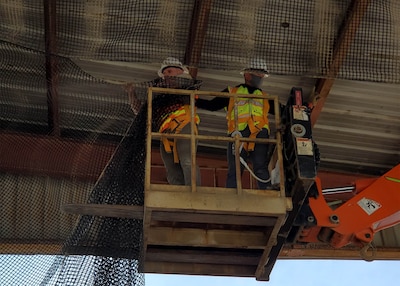 Jhunar Medenilla, right, helps Ted Adams, as the pair continues to hang netting to keep out birds who were nesting above a receiving area at DLA Disposition Services at Camp Arifjan.