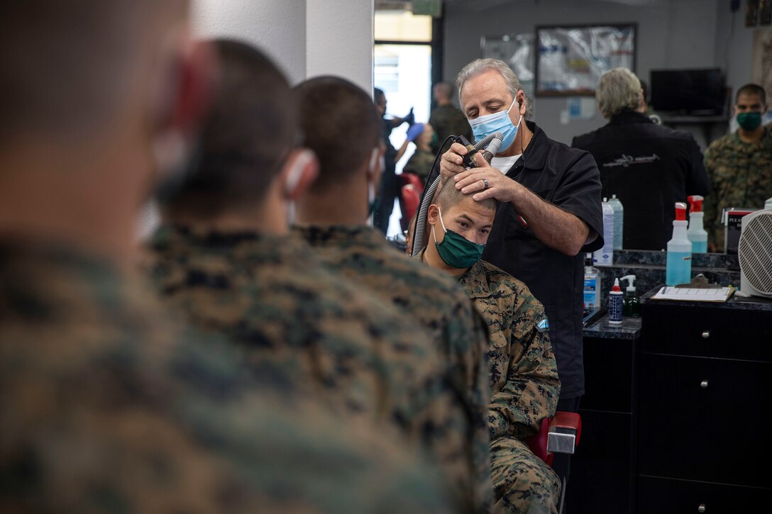 A barber shaves a Marine Corps recruit's head as others stand in line and watch.