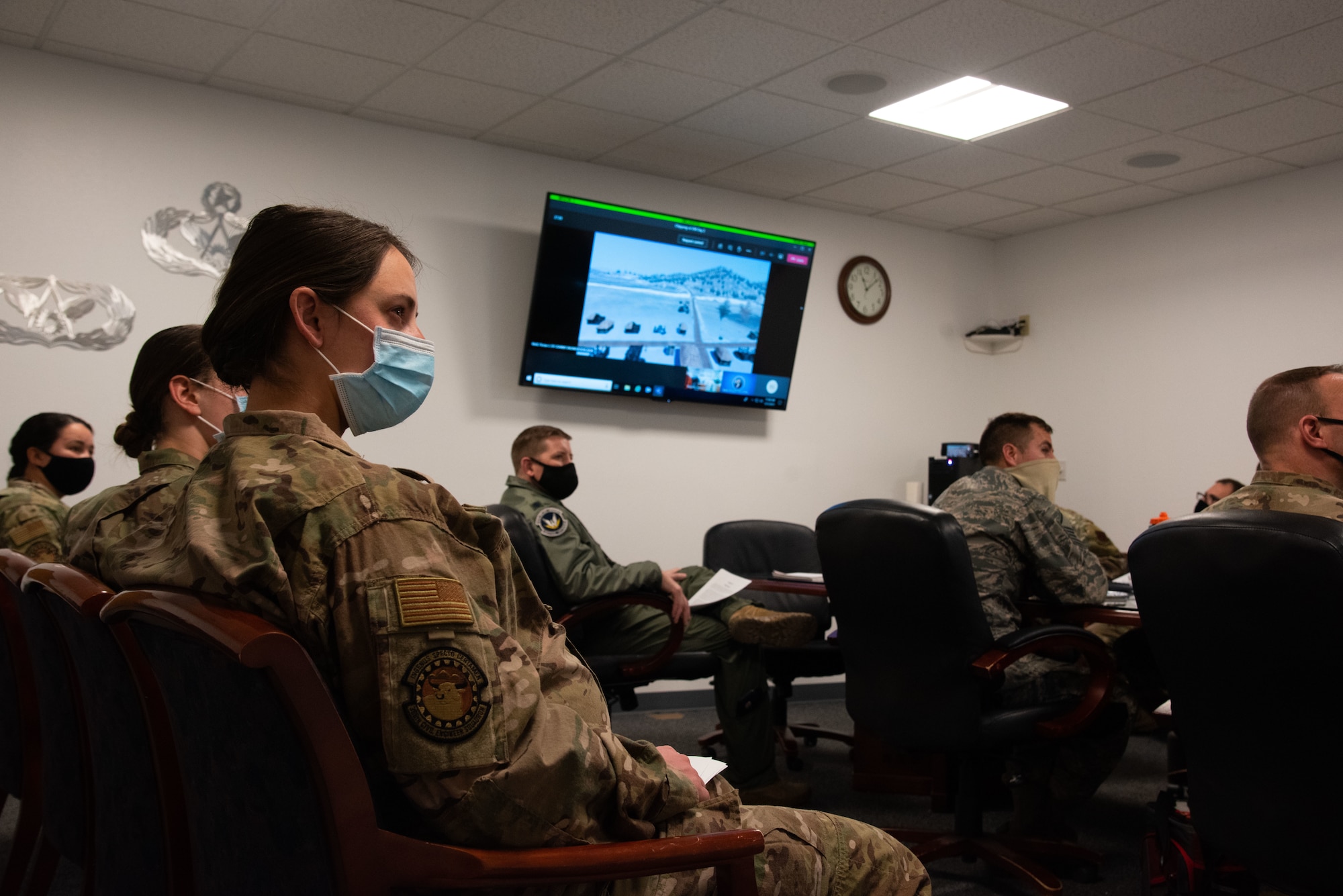 Airmen sit in a room and look at a screen. They are sitting in on a virtual staff ride.