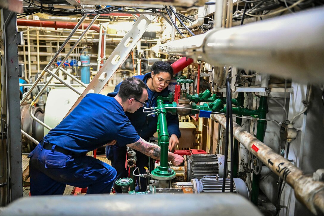 Two Coast Guardsmen perform maintenance on a ship.