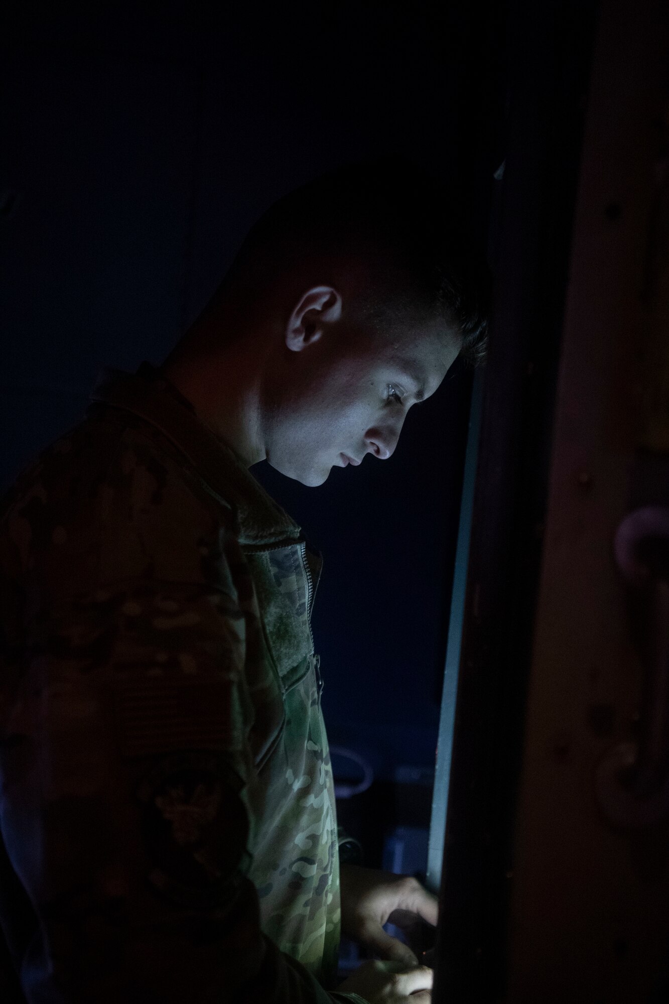 A loadmaster looks down at a screen while inputting data in the back of a C-130.