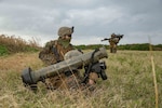 Three Marines take part in an exercise in a field, two of them holding large weapons.