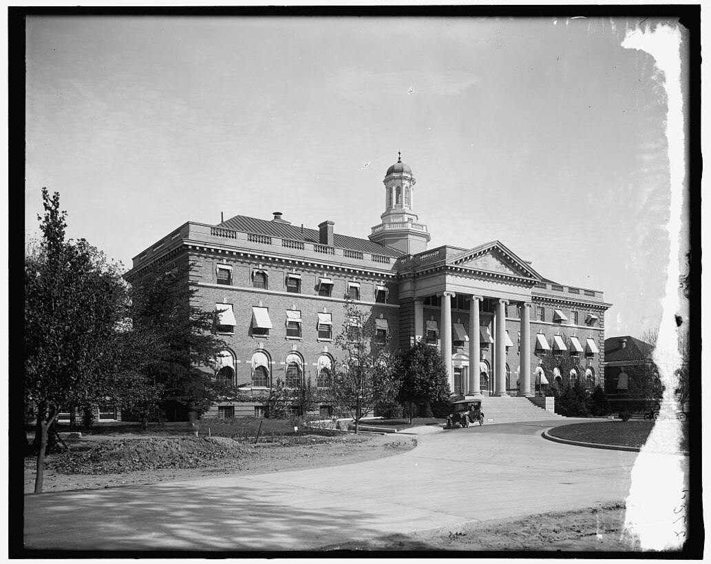 A large building with columns sits on a plot of land.