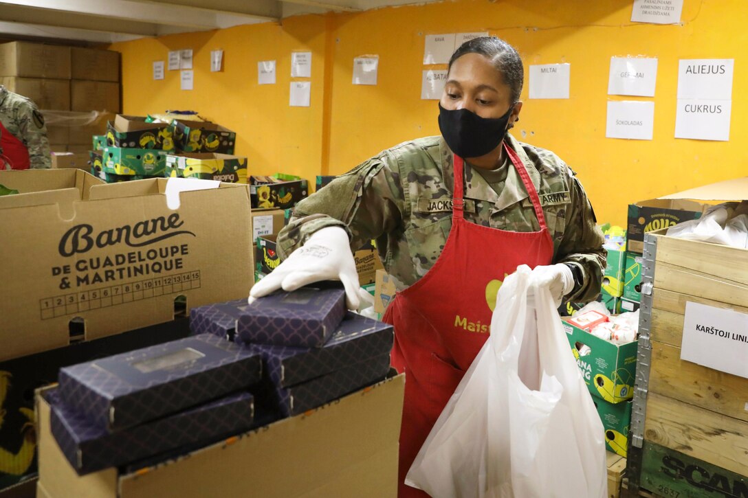 A soldier holds a box and plastic bag in a food bank.