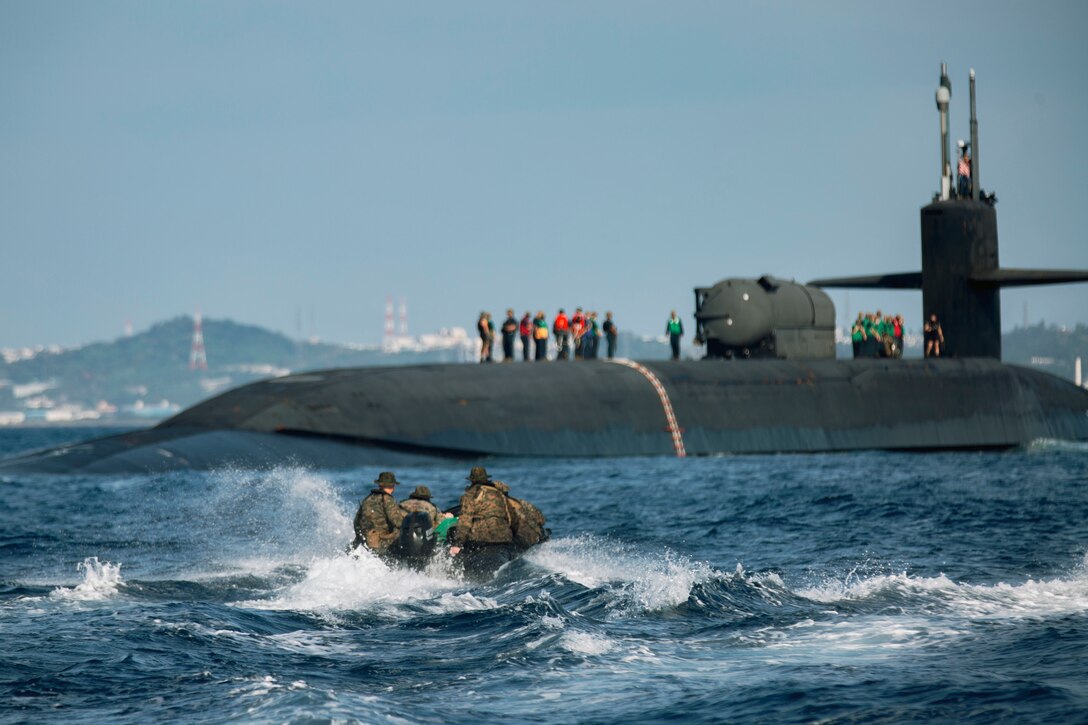 Marines in a rubber raft approach a submarine.