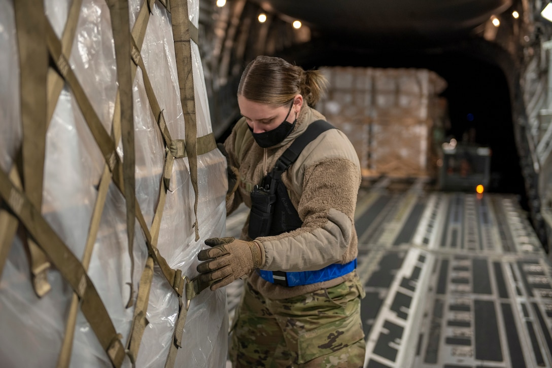An airman secures a pallet of cargo inside an aircraft at night.