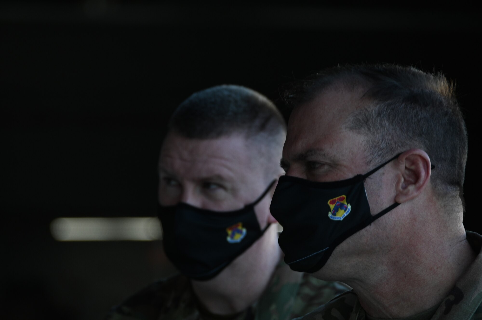 Two men in military uniforms and similar masks look intensely at an unknown source.
