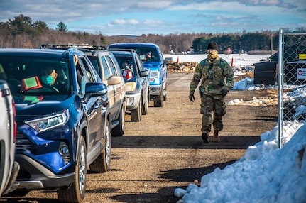 Staff Sgt. Ryan Gilbert, a combat engineer from the Connecticut National Guard's 192nd Engineer Battalion, walks down a line of cars to check on the passengers after receiving the COVID-19 vaccination at Rentschler Field in East Hartford, Jan. 4, 2021.