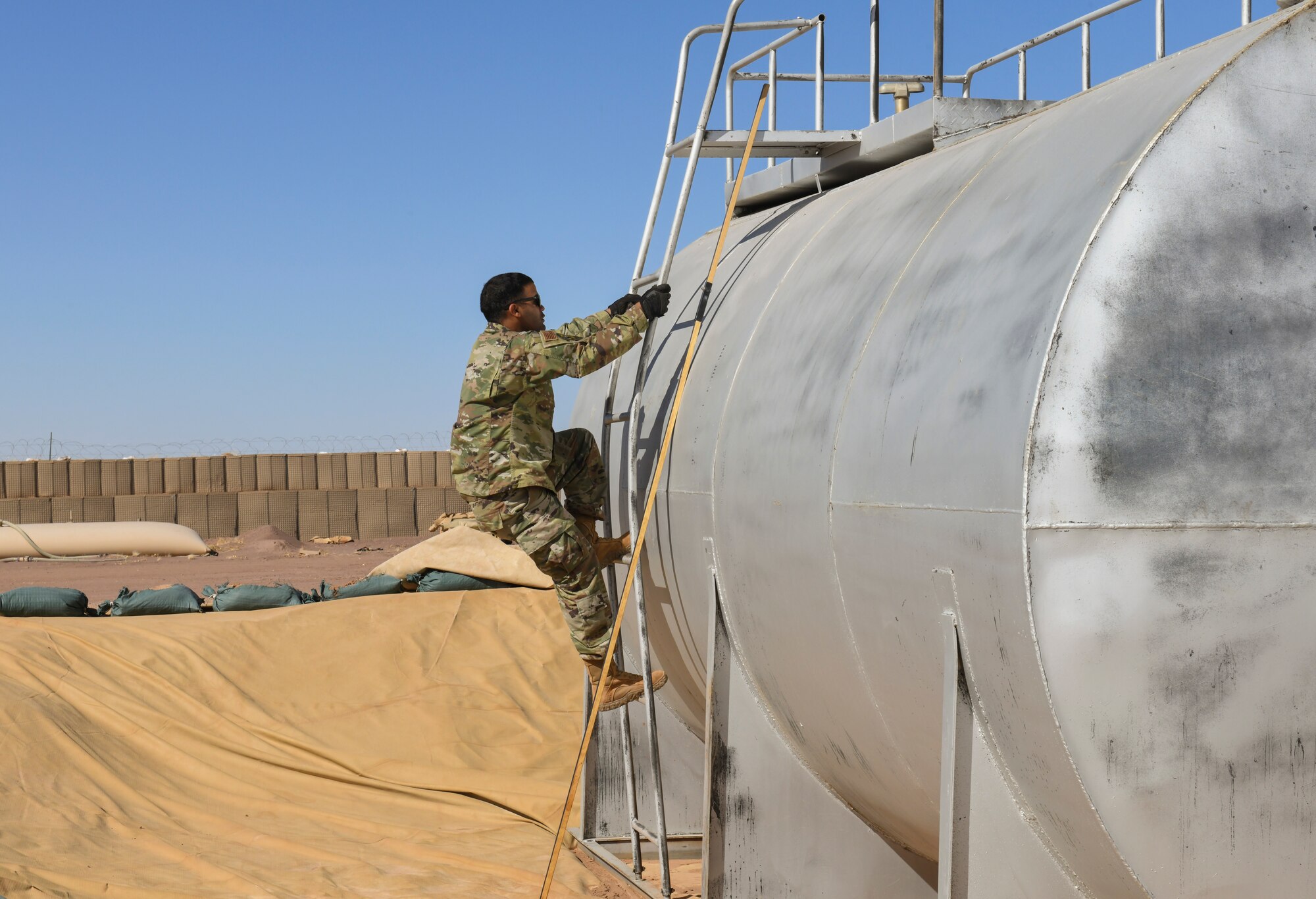 U.S. Air Force Staff Sgt. Josue Ruiz-Garcia, 724th Expeditionary Air Base Squadron fuel operations noncommissioned officer in charge, climbs a fuel tank to get an accurate read on the volume of fuel at Nigerien Air Base 201, Agadez, Niger, Feb. 2, 2021. This process allows the petroleum, oils, and lubrication fuels Airmen to accurately account for all the fuel they have on base. (U.S. Air Force photo by Senior Airman Gabrielle Winn)