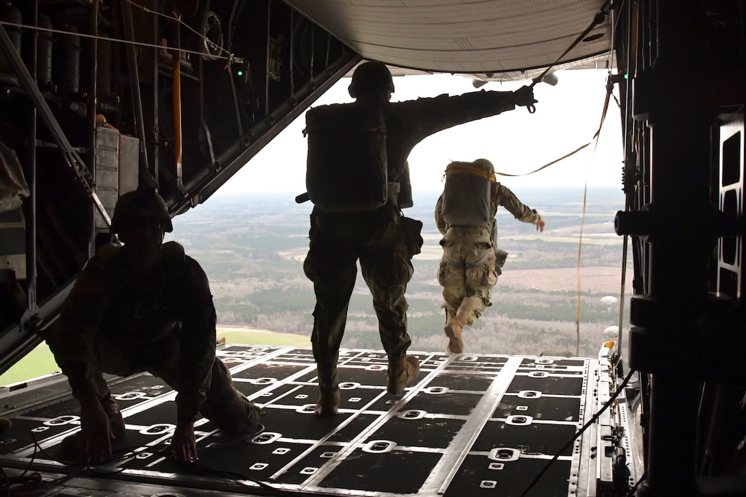 Soldiers stand in line to jump out of an airborne aircraft.