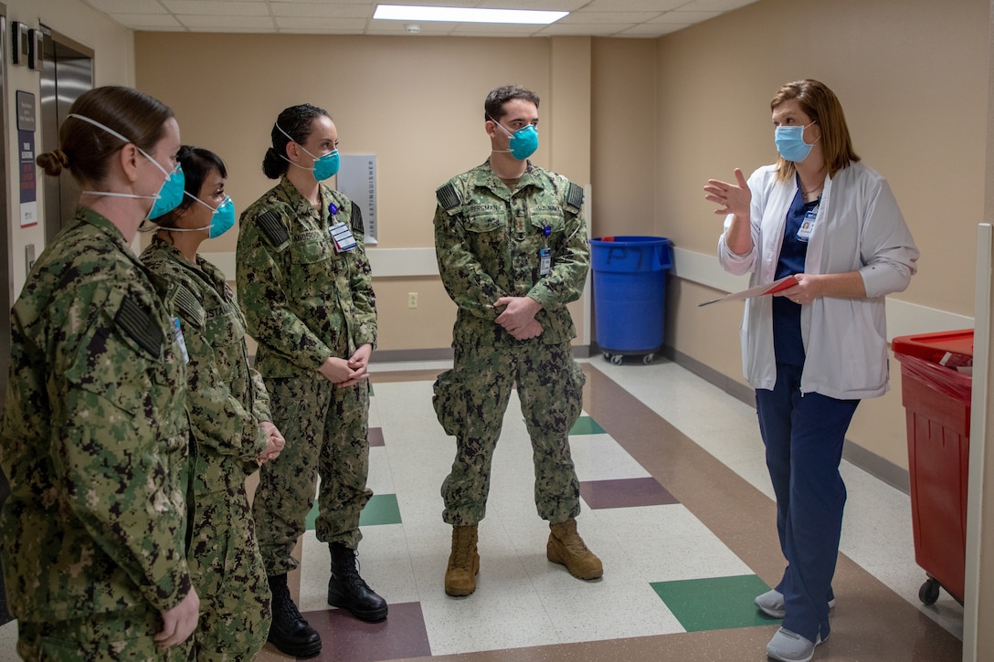A nurse wearing a face mask speaks to four Navy nurses wearing face masks