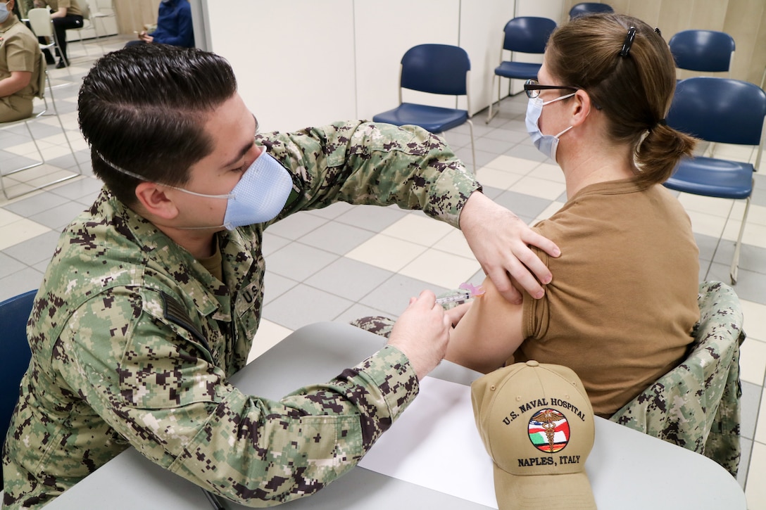 A sailor wearing a face mask gives a Navy officer a COVID-19 vaccine.