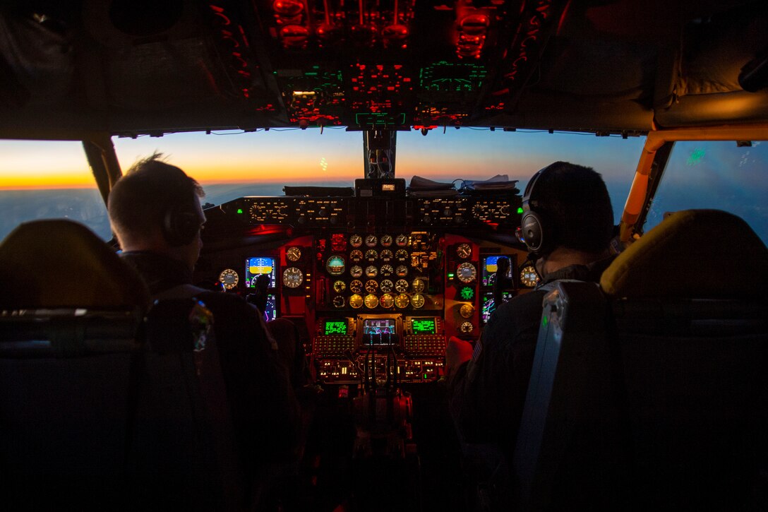 Two pilots sit in a cockpit illuminated by colorful lights.