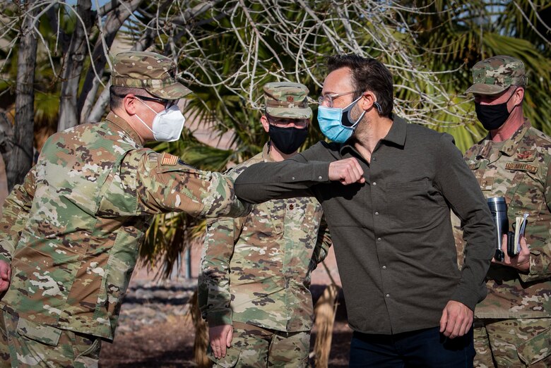 a civilian man and an Airmen tap elbows to greet each other