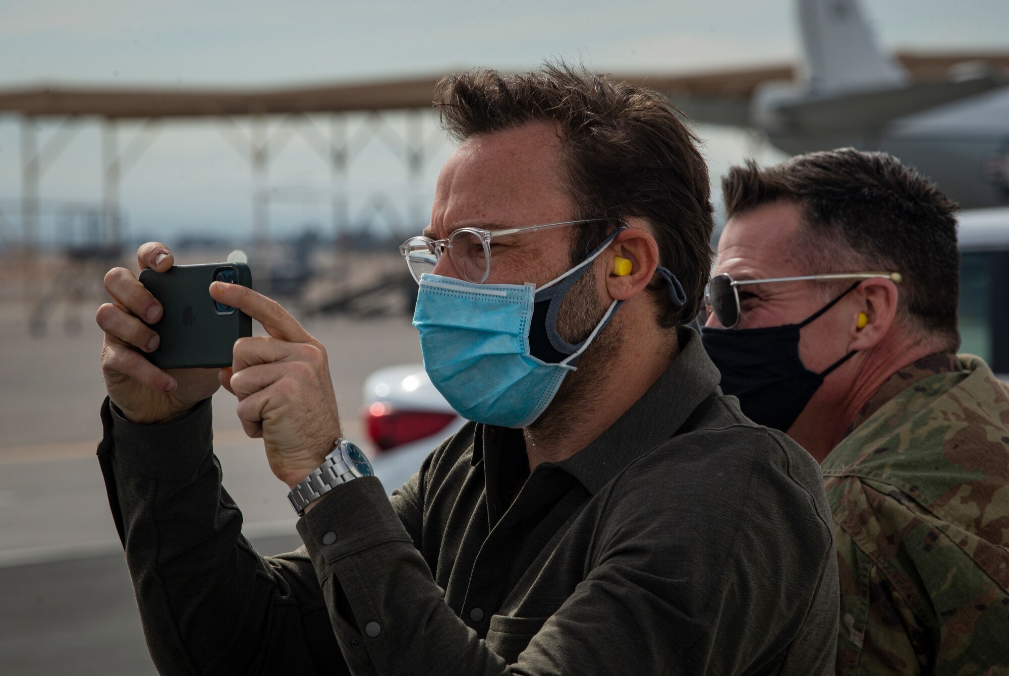 man in mask takes photo with cell phone on flight line