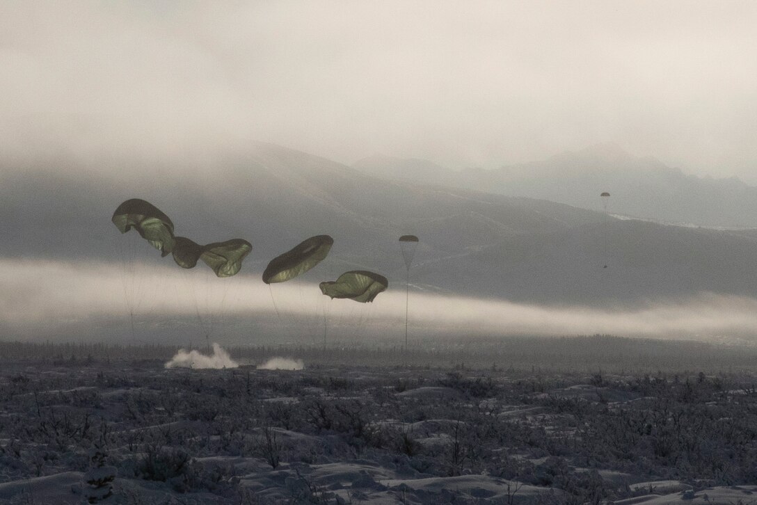 Airmen freefall with parachutes in a field.