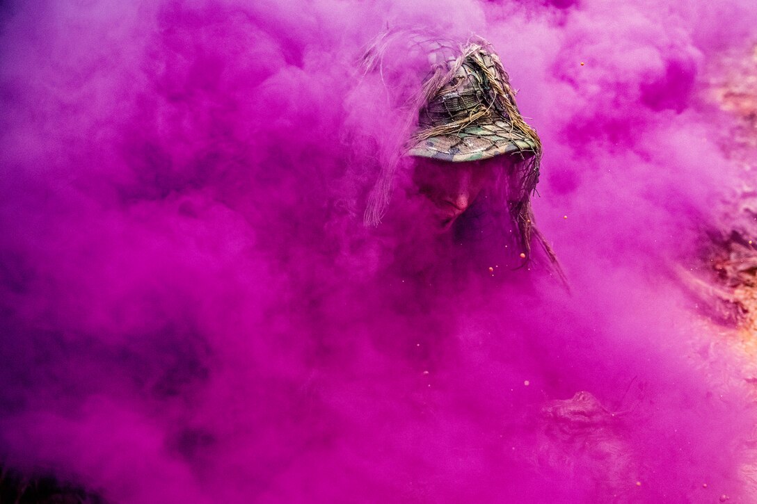 A soldier's face half-emerges from a big cloud of pinkish-purple smoke.