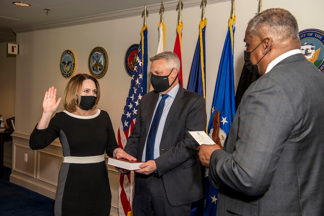 Secretary of Defense Lloyd J. Austin III stands facing Dr. Kathleen H. Hicks, who holds up her right hand and places her left hand on a book.