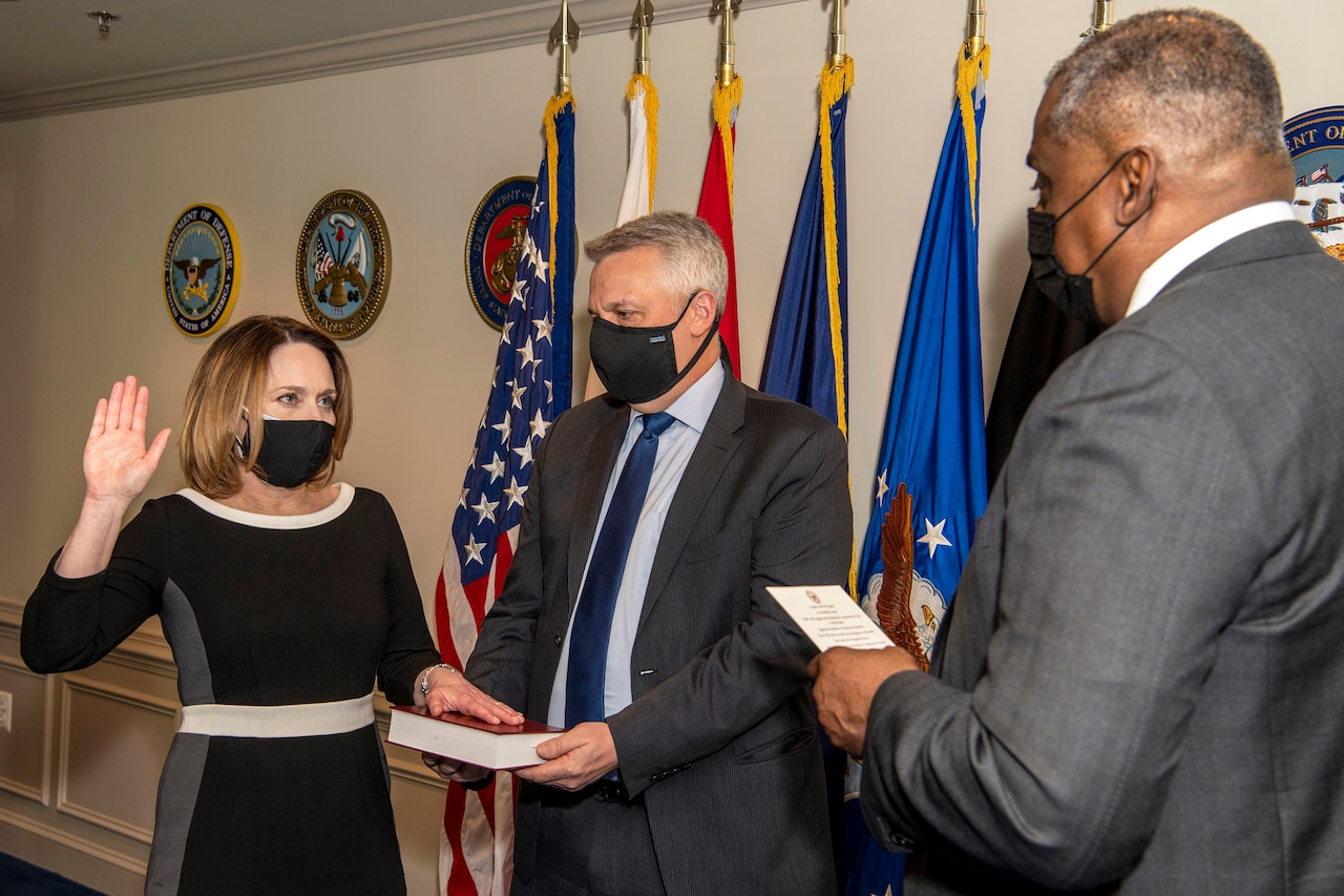 Secretary of Defense Lloyd J. Austin III faces Dr. Kathleen H. Hicks, who raises her right hand and puts her left hand on a book.