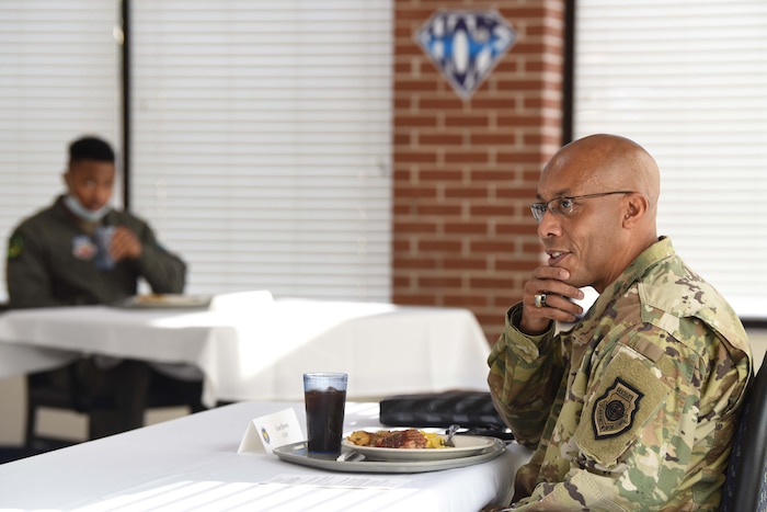 Photo shows people sitting at separate tables speaking while eating lunch.