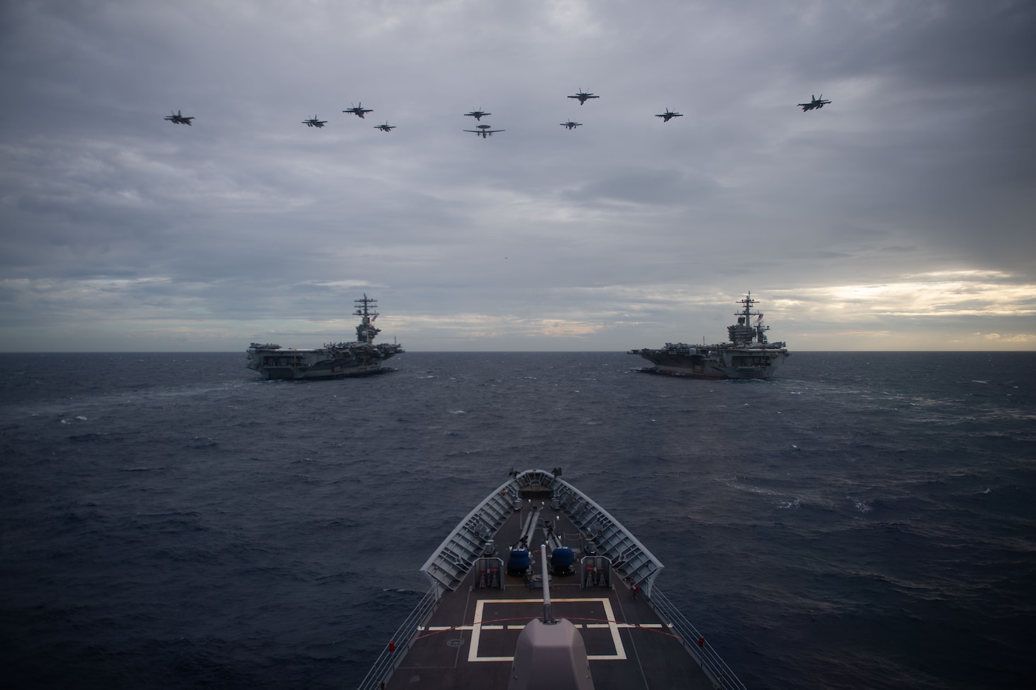 Aircraft from Carrier Air Wings (CVW) 17 and 11 fly in formation above the aircraft carriers USS Nimitz (CVN 68), left, and USS Theodore Roosevelt (CVN 71) during dual carrier operations as seen from the guided-missile cruiser USS Princeton (CG 59). The Nimitz and Theodore Roosevelt Carrier Strike Groups are conducting dual carrier operations in the Indo-Pacific in support of maritime security operations and theater security cooperation efforts.