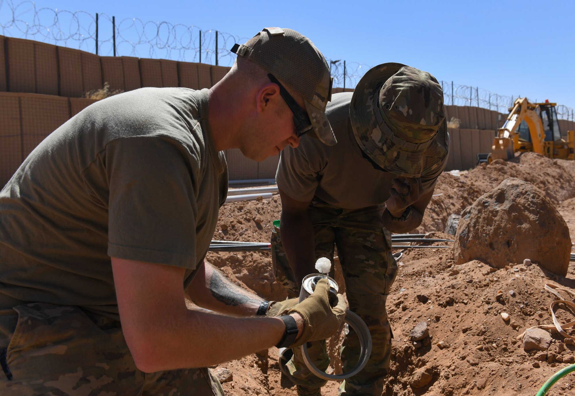 U.S. Air Force Tech. Sgt. Jessie Correia, left, 724th Expeditionary Air Base Squadron civil engineer electrical systems supervisor, and Tech. Sgt. Edward George, 724 EABS CE electrical systems craftsman, prepare to apply adhesive to new polyvinyl chloride conduit at Nigerien Air Base 201, Agadez, Niger, Feb. 4, 2021. The adhesive used creates a solid bond for electrical PVC conduit pieces. (U.S. Air Force photo by Senior Airman Gabrielle Winn)