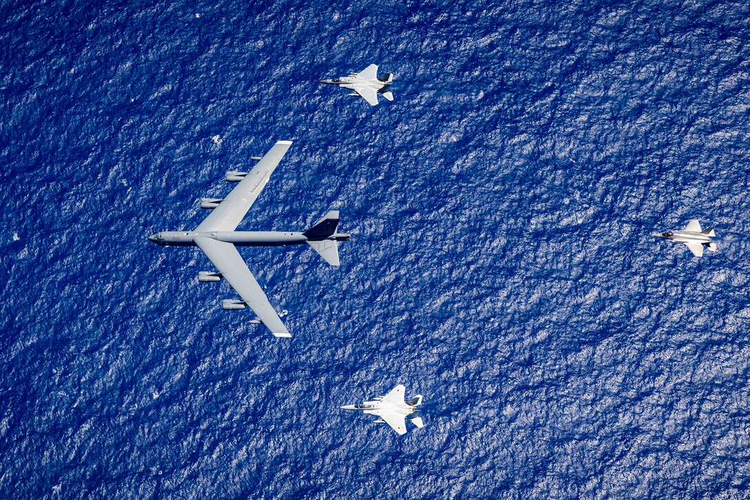 Four U.S. and Japanese air force aircraft fly in a diamond formation over vivid blue water.