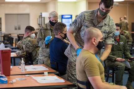 Staff Sgt. Katie Farrell and Staff Sgt. Ian Miller, standing, administer the Pfizer COVID-19 vaccine to Airmen in the 167th Airlift Wing dining facility Feb. 6, 2021. Farrell and Miller are members of the 167th Medical Group serving in the West Virginia National Guard’s Task Force Medical-East.