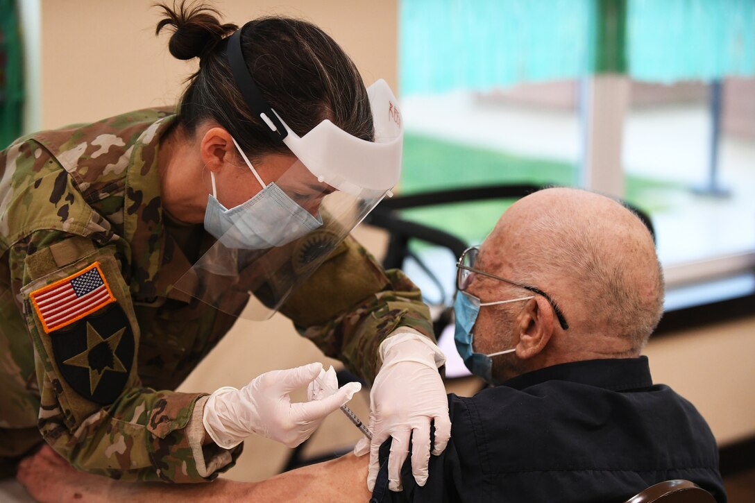 A soldier wearing a face mask and gloves gives a COVID-19 vaccine to an elderly man