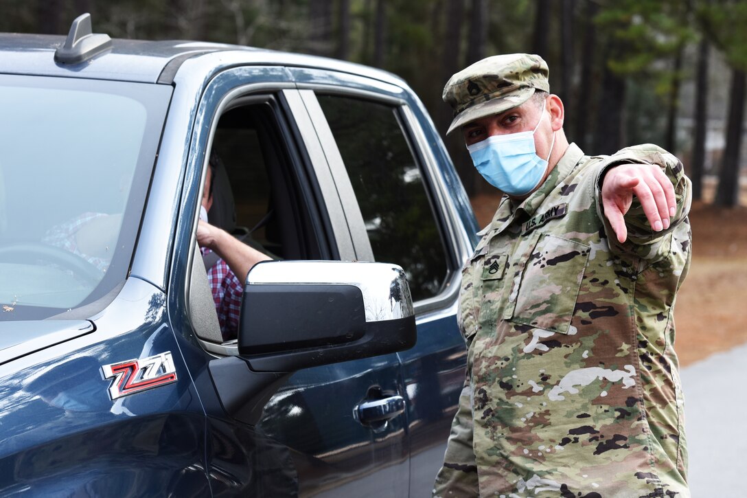 A soldier wearing a face mask directs a vehicle to the COVID-19 mobile testing site