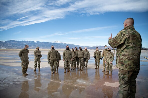 An Airman speaks to a small audience of soldiers on the flight line with Pikes Peak in the background.
