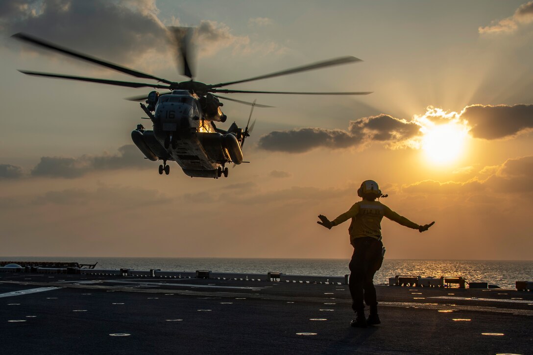 A sailor signals a helicopter to land on a ship.