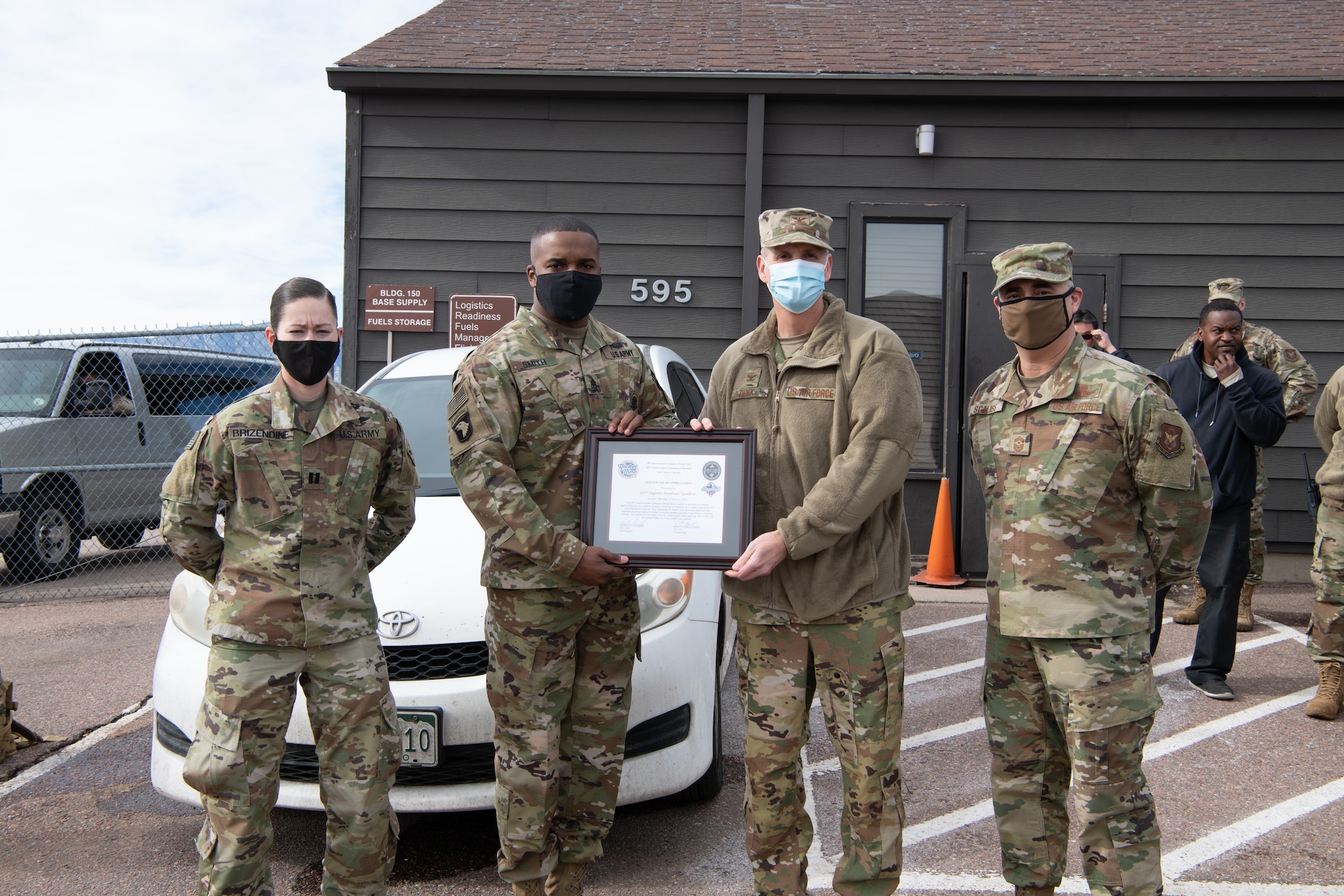 Two soldiers present a certificate of appreciation to two Airmen with a small audience in the background.