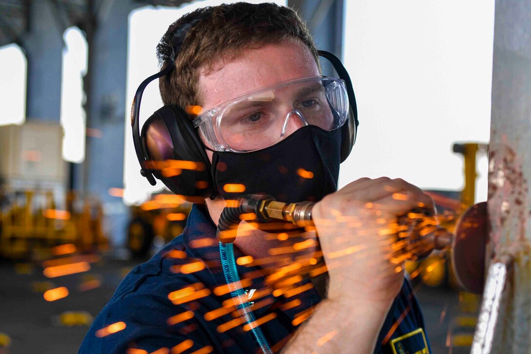 A sailor uses a grinder on a metal pole as sparks fly.