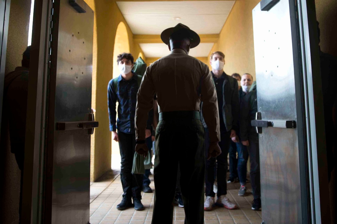 A Marine stands in front of two lines of recruits.
